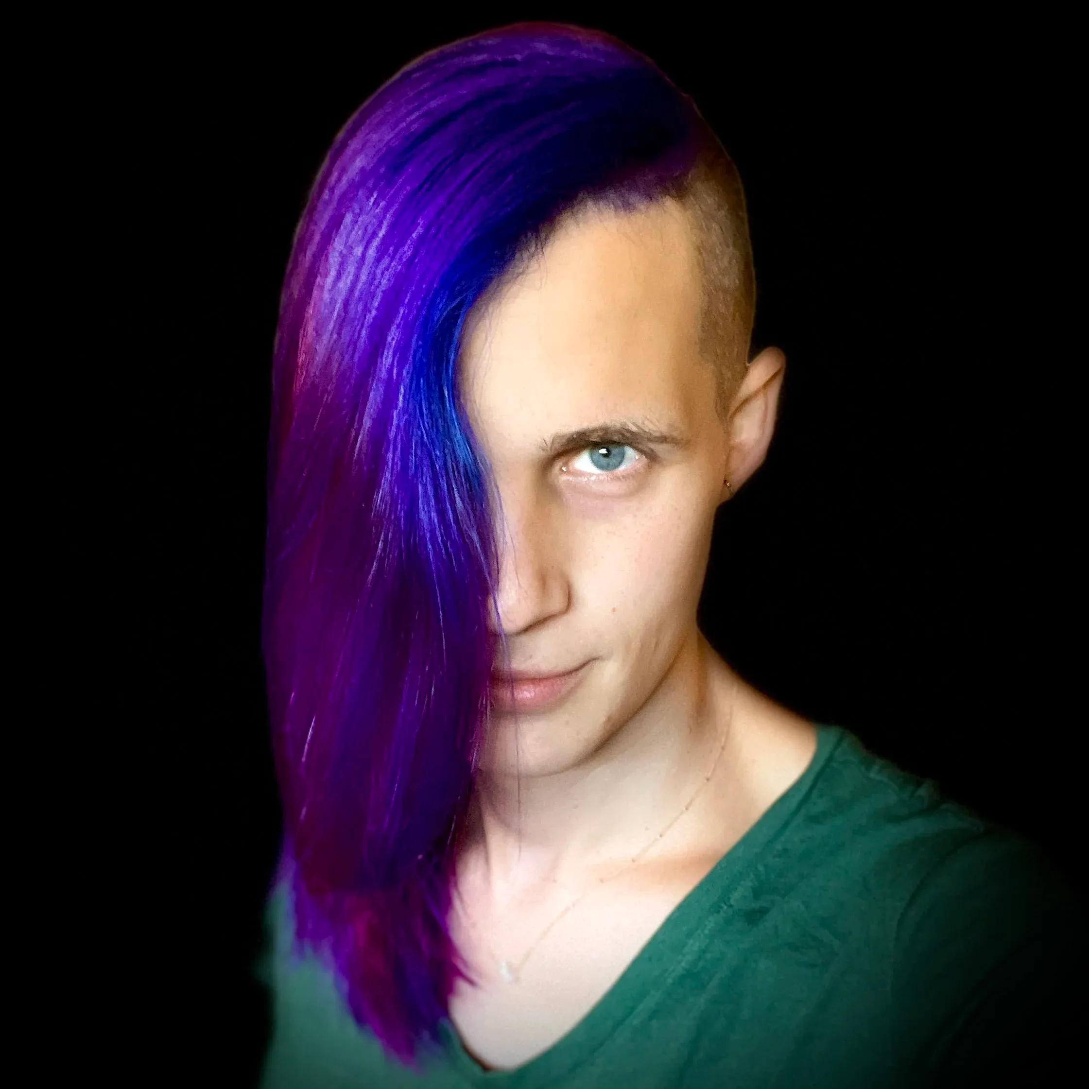 Cassie McBride, with long purple hair swept across one side of her face, looking towards the camera against a dark background